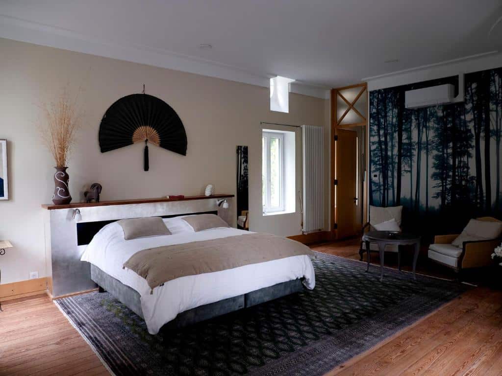Spacieuse chambre d'hôtel moderne avec grand lit, tête de lit en bois, décoration murale éventail et fresque de forêt.