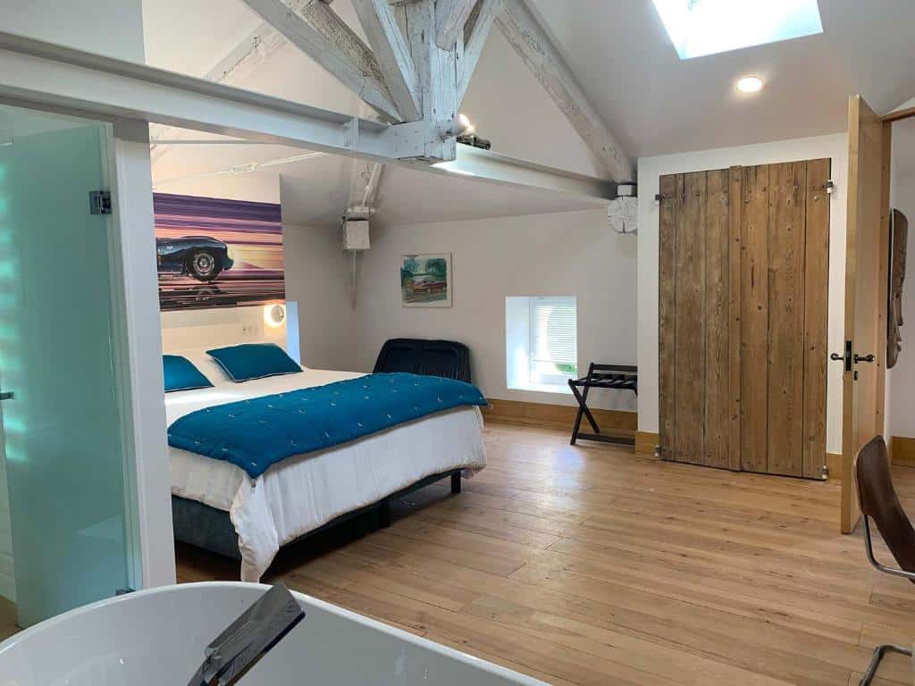 Chambre moderne esprit loft avec lit double, fresque murale voiture vintage bleue, poutres apparentes, baignoire îlot et porte coulissante bois.